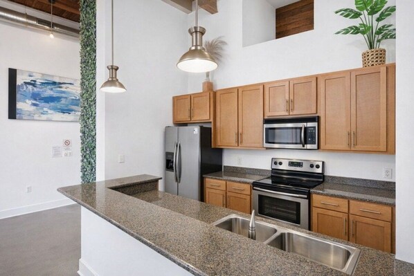 A modern kitchen with granite countertops, stainless steel appliances, wooden cabinets, and pendant lighting.