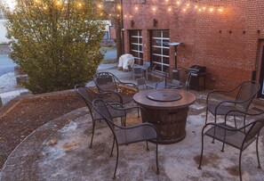 Un patio al aire libre con una mesa redonda y sillas, una parrilla y luces colgantes.
