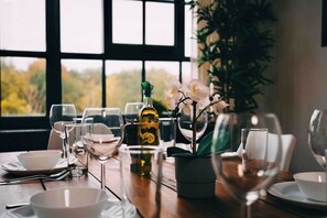 Mesa de comedor servida con copas de vino, una botella y una orquídea en maceta.