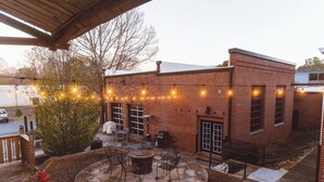 An outdoor patio area with a brick building, string lights, and a fire hydrant. - Cozy mill loft w/ 2 king beds, gym & pool (Spartanburg)