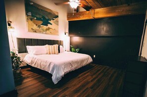 A bedroom with a bed, a headboard, a wall-mounted TV, and a ceiling fan. - Cozy mill loft w/ 2 king beds, gym & pool (Spartanburg)