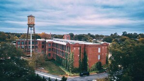 A large brick building with a water tower, surrounded by trees and a clear sky. - Cozy mill loft w/ 2 king beds, gym & pool (Spartanburg)
