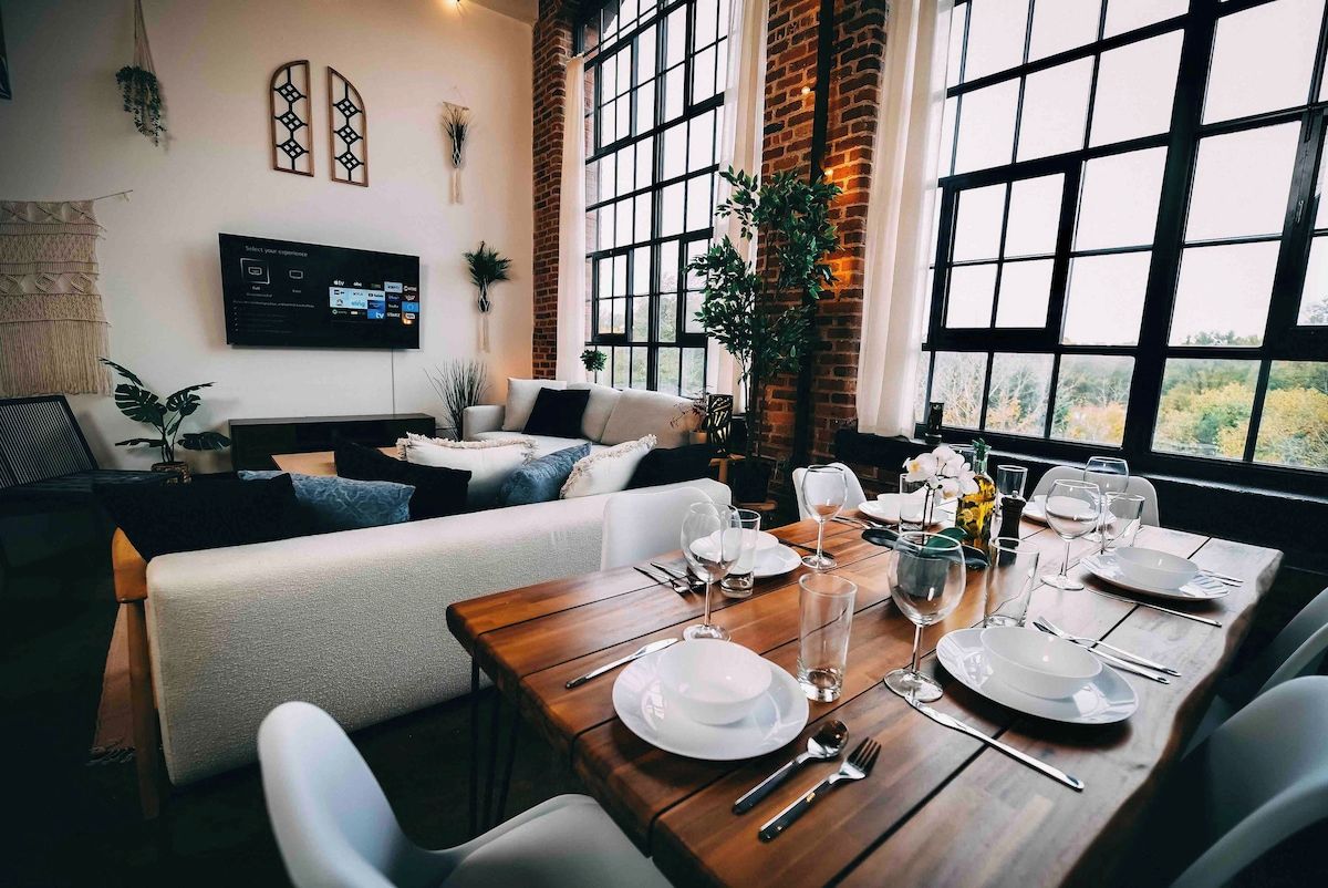 A dining area with a wooden table set for four, a sofa, and a TV mounted on the wall.