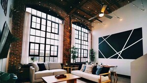 A modern living room with a brick wall, large windows, a sofa set, a coffee table, and a geometric wall art piece.