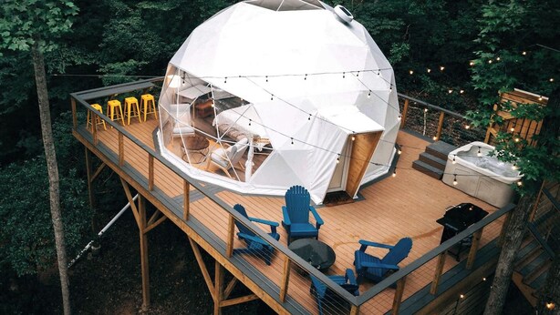 Una tienda en forma de cúpula con una terraza de madera, mobiliario exterior y un jacuzzi.