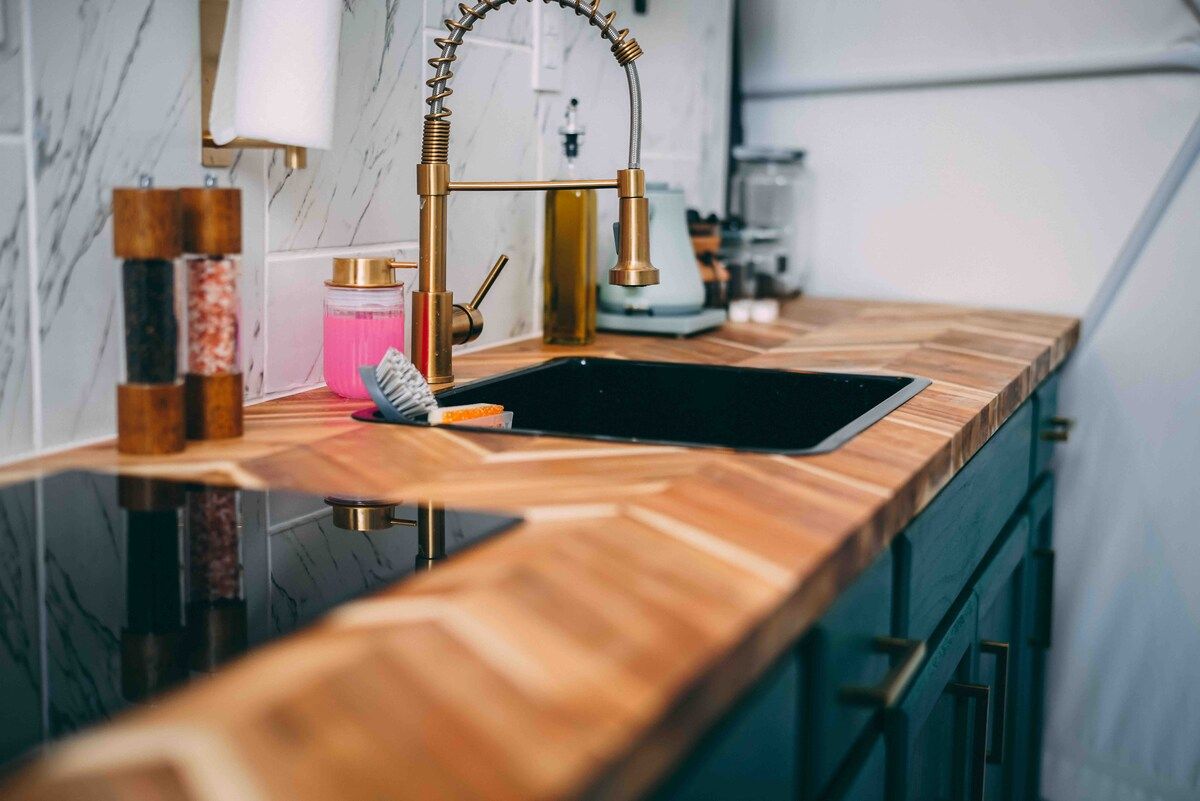 A kitchen with a wooden countertop, a gold faucet, and a black sink.