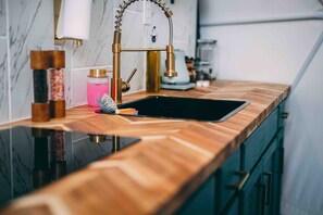 A kitchen with a wooden countertop, a gold faucet, and a black sink.