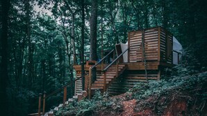 A wooden cabin with a staircase leading to a deck surrounded by forest.