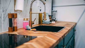 A kitchen with a marble backsplash, a wooden countertop, and a gold faucet.