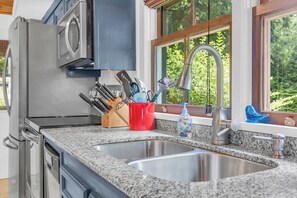 A kitchen with a stainless steel sink, a window with a view of greenery, and a knife block with utensils. - Lakefront Cabin w/ Hot Tub & Stunning Views (Lyman)
