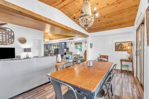 Un coin repas avec une table et des chaises en bois, un lustre et une cuisine en arrière-plan.