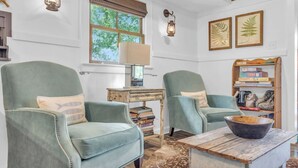 A cozy room with two green armchairs, a wooden table, a bookshelf, and a window with blinds. - 3/2 Lake Front - Hot Tub - 2 King Beds - Sleeps 8 (Lyman)