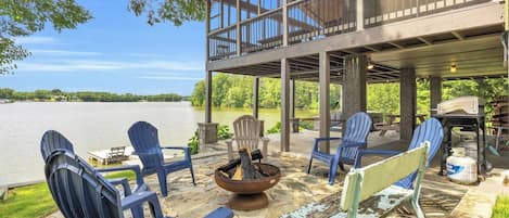 An outdoor deck with Adirondack chairs, a fire pit, and a view of a lake.