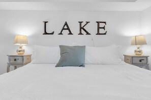 Un lit avec une literie blanche, un seul oreiller bleu et deux tables de chevet avec des lampes.