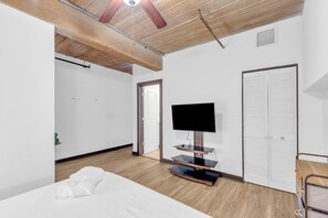 Une chambre à coucher avec un lit, un téléviseur posé sur un meuble, une armoire et un ventilateur de plafond.