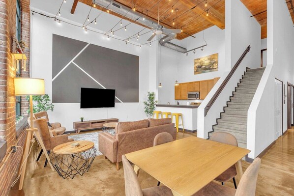 Un intérieur moderne comprenant un coin repas, des canapés, un téléviseur et un escalier.