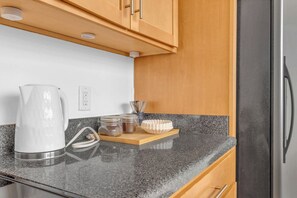 A kitchen with a granite countertop, a kettle, a coffee maker, a toaster, and a refrigerator.