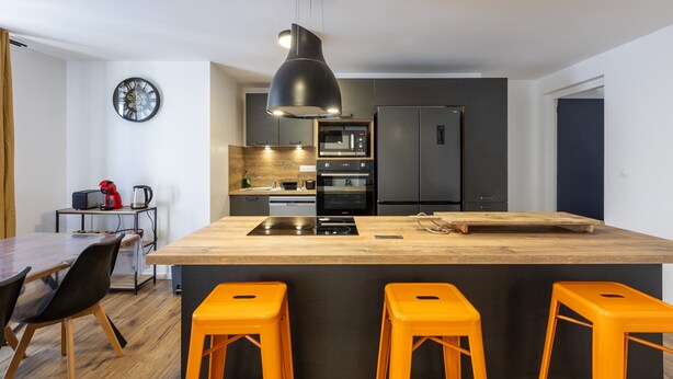 Una cocina moderna con una isla central, armarios negros y encimera de madera.