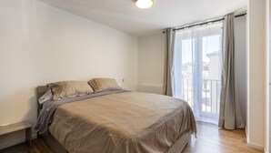 Un dormitorio con cama, mesita de noche, ventana con cortinas y vistas al exterior.