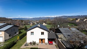 Un barrio residencial con casas, un coche rojo estacionado frente a una vivienda y montañas nevadas al fondo.