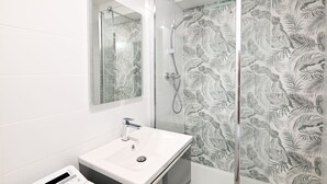 Een badkamer met een douchecabine van glas, een witte wastafel en een spiegel.