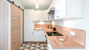 Een kleine keuken met witte kasten, een houten aanrechtblad en een vloer van honingraat tegels.