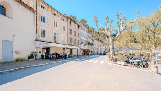 A street with cafes, outdoor seating, and a pedestrian crossing.