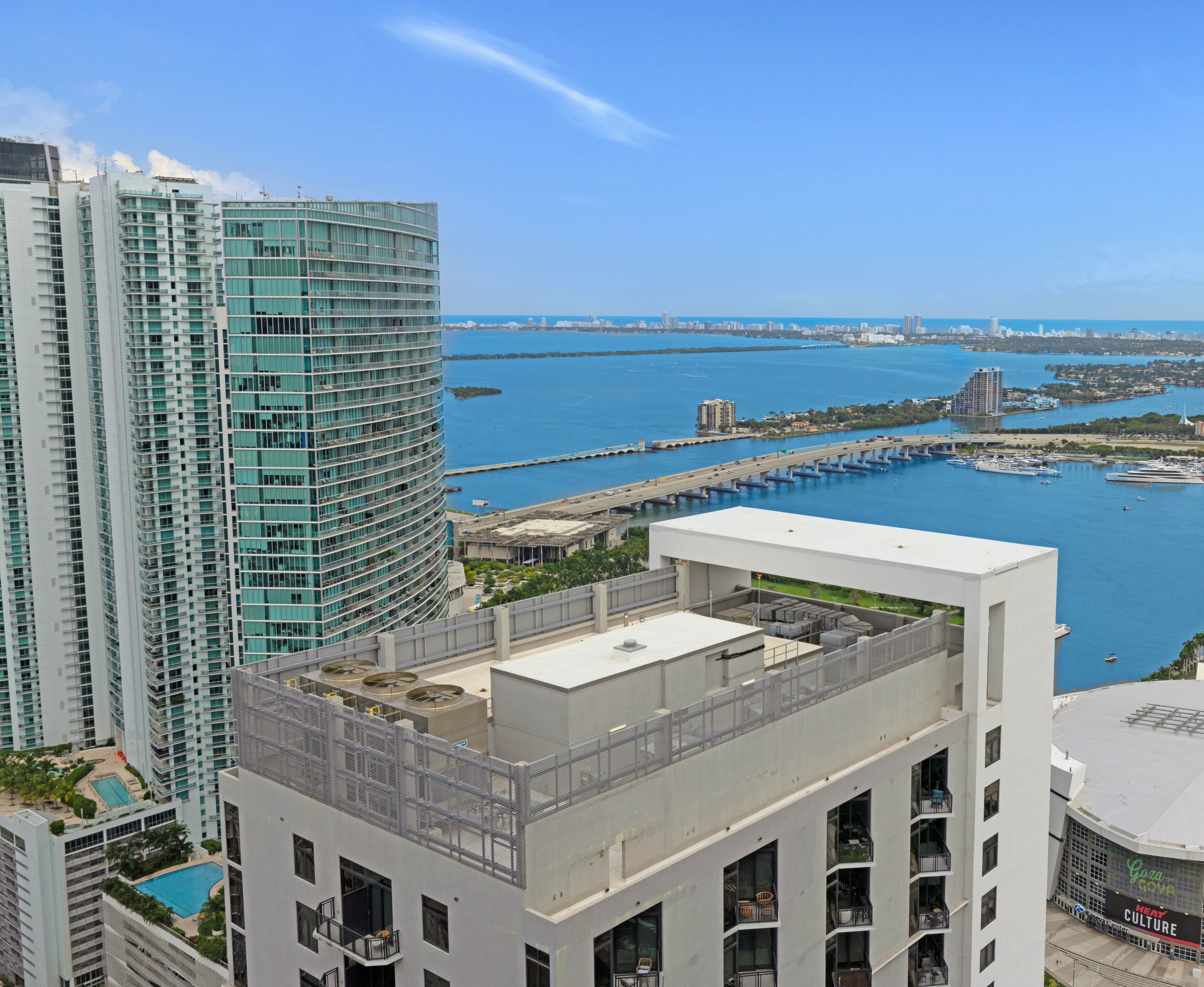 A high-rise building with a rooftop terrace, a view of a marina with boats, and a distant city skyline.