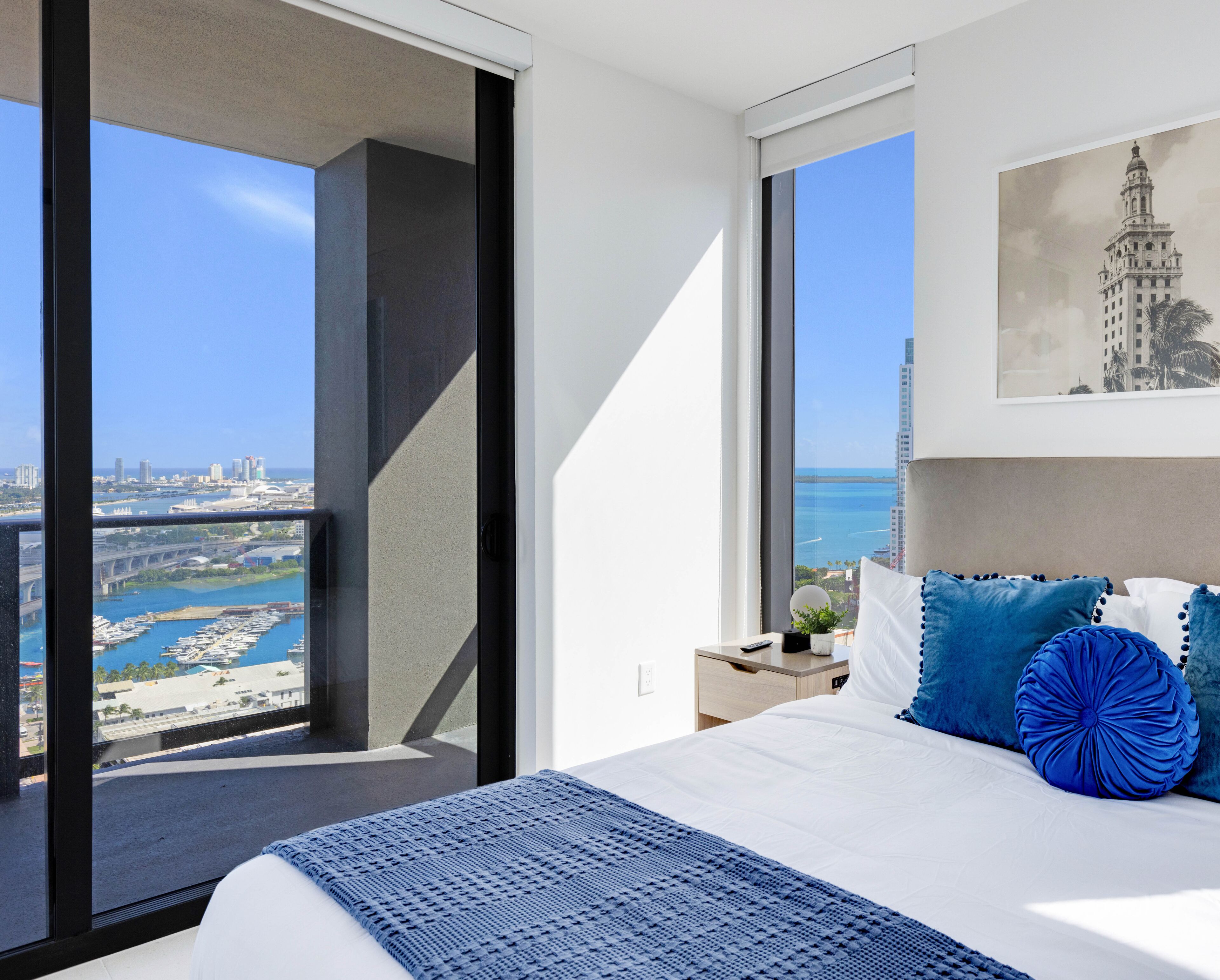 A hotel room with a large bed, a view of the city and ocean, and a balcony.