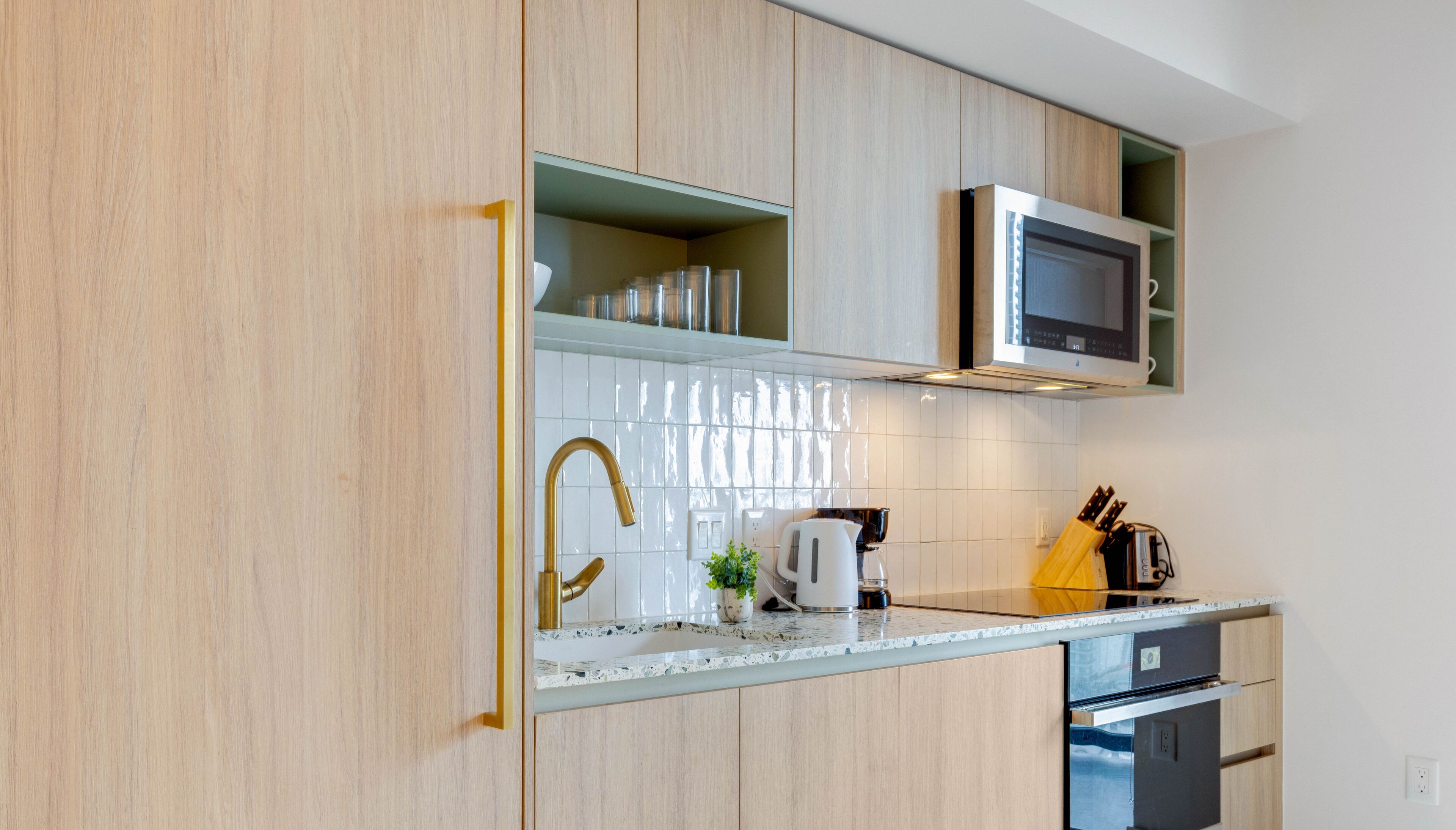 Een moderne keuken met houten kastjes, een roestvrijstalen magnetron, een spoelbak en een aanrecht met waterkoker en messen.