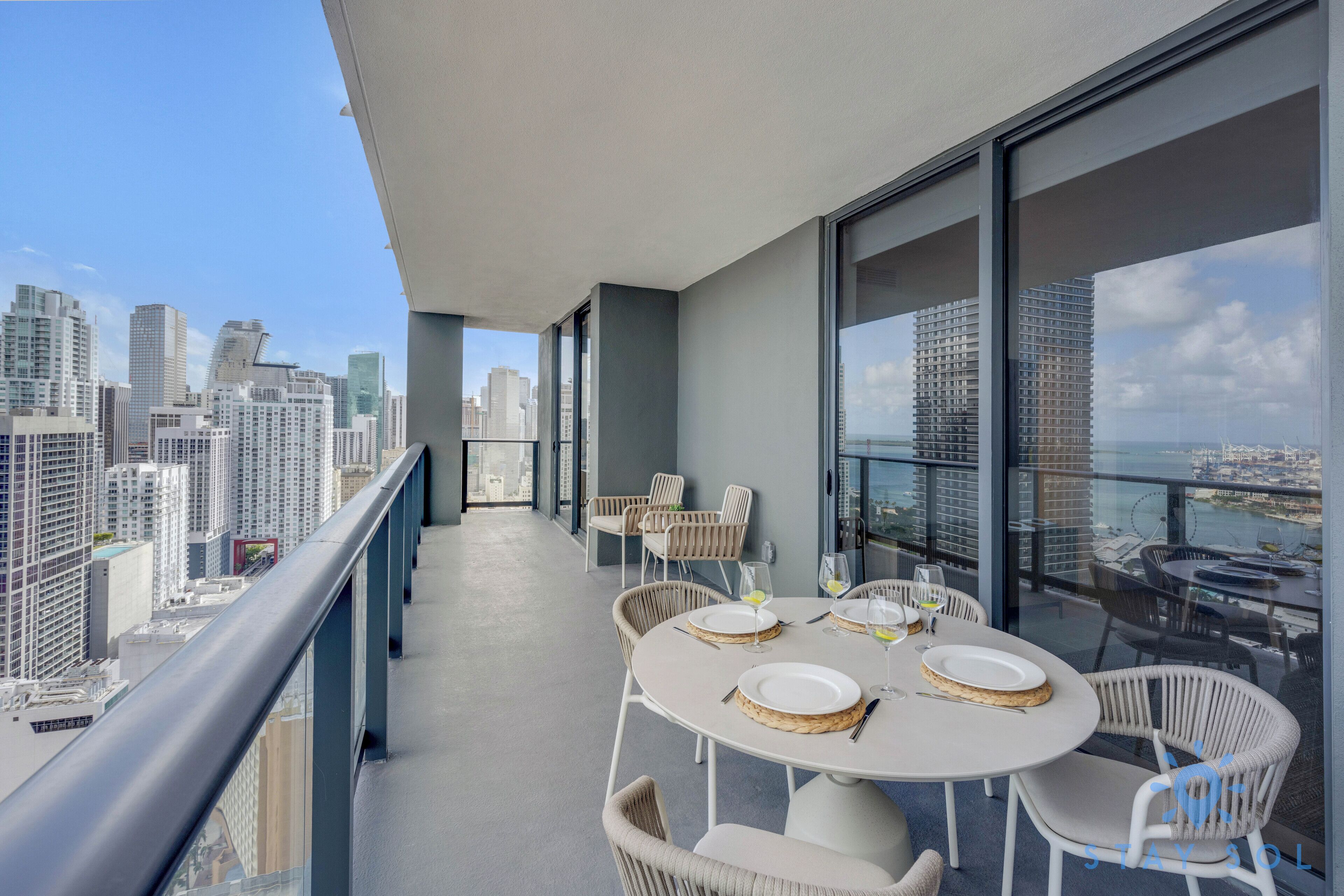 Uma varanda com mesa redonda posta para refeições, com vista para um horizonte urbano repleto de arranha-céus.