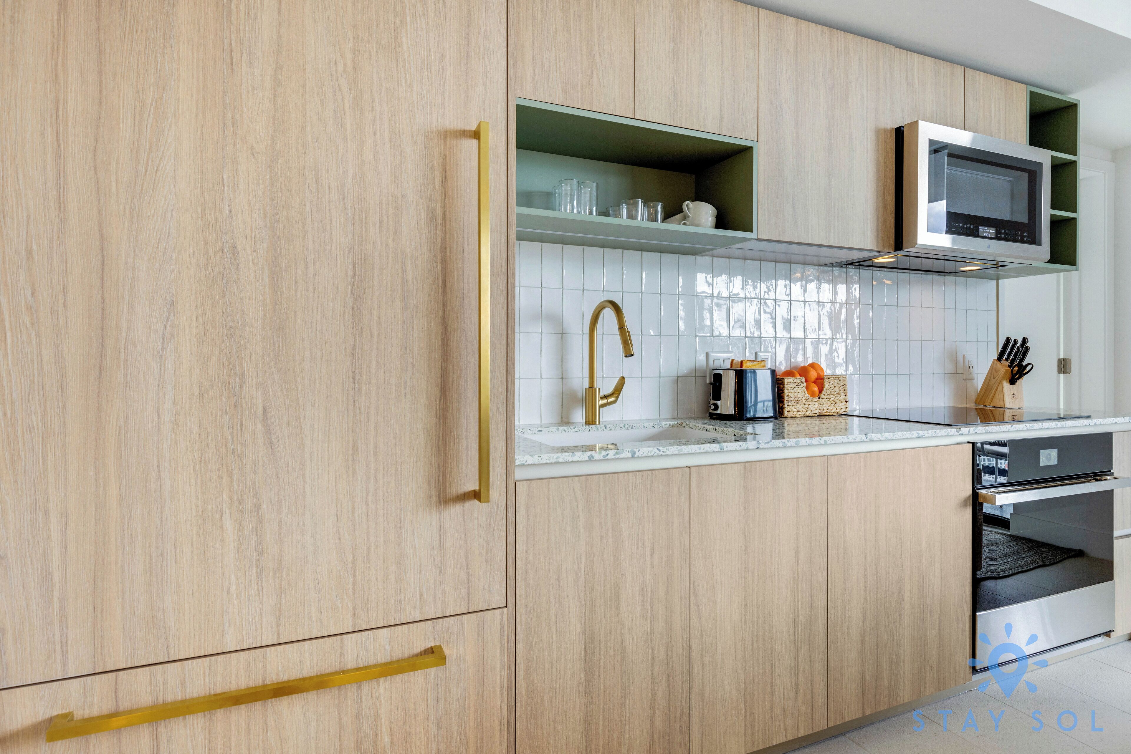 Una cocina moderna con armarios de madera clara, un microondas de acero inoxidable y un salpicadero de vidrio.