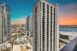 A high-rise building with multiple balconies, a swimming pool, and a view of a body of water and a stadium in the background. - Stay Sol Downtown (Miami)
