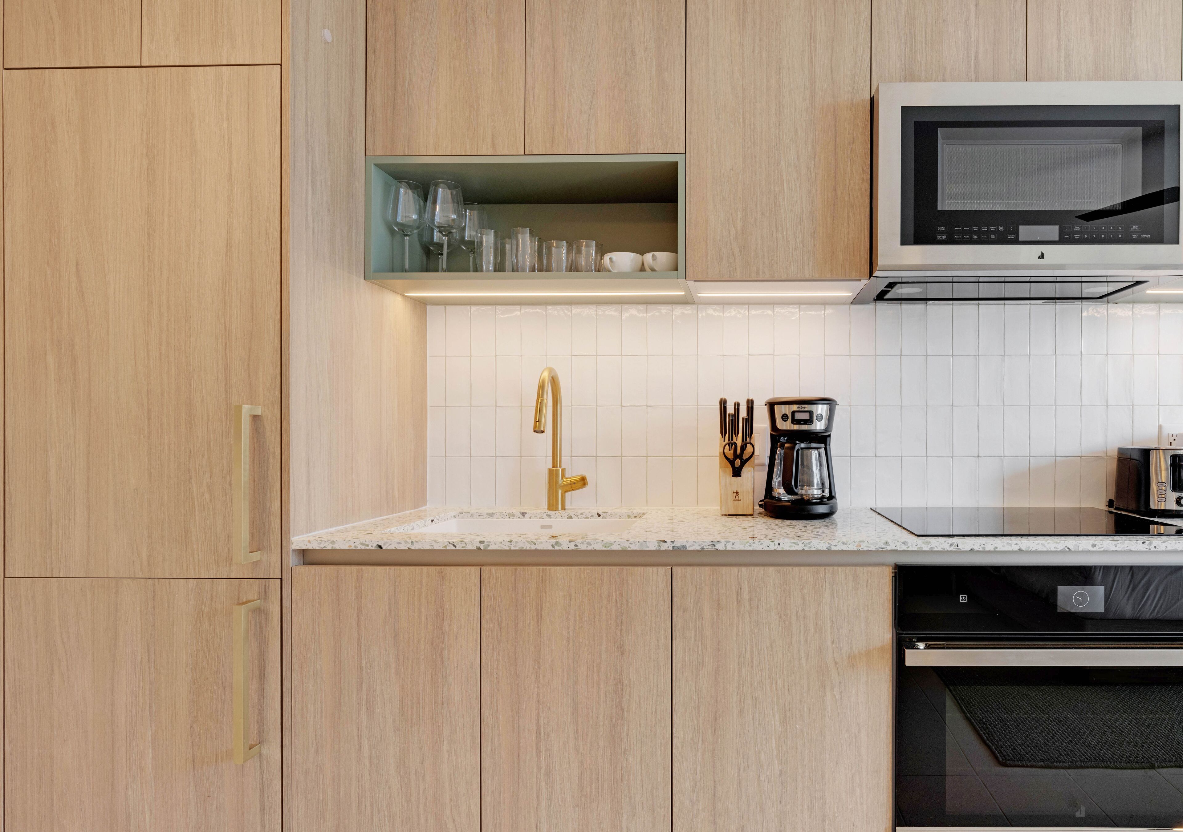 A modern kitchen with wooden cabinets, a gold faucet, a microwave, and a coffee maker.