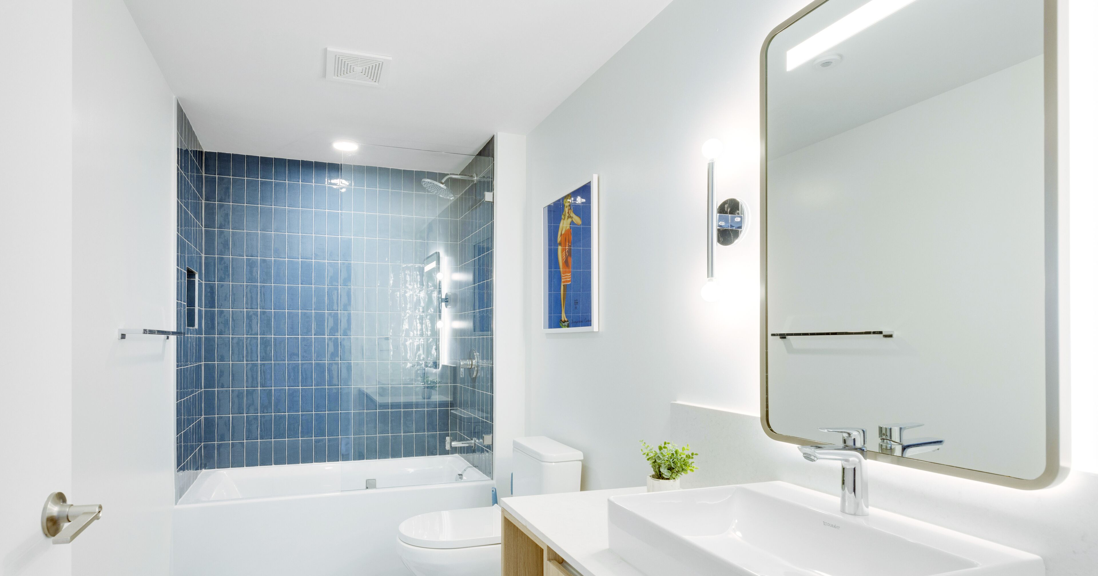 A modern bathroom with a bathtub, toilet, and sink, featuring blue tiles and a large mirror.