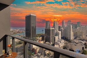 Blick auf eine Stadtlandschaft vom Balkon aus, mit Sonnenuntergang, hoch aufragenden Gebäuden und einer Uferpromenade.