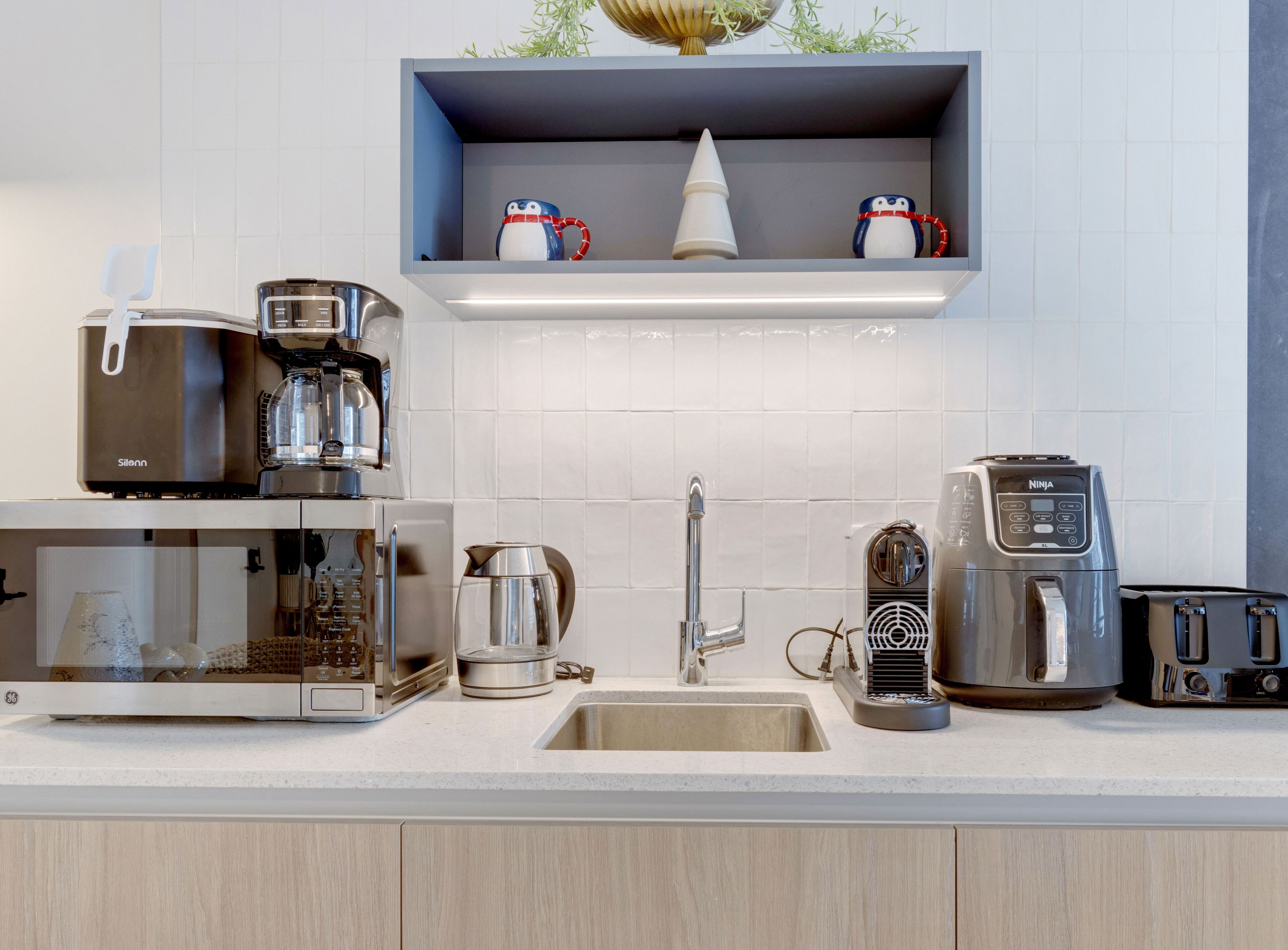 A modern kitchen with a coffee maker, toaster, kettle, and a sink.