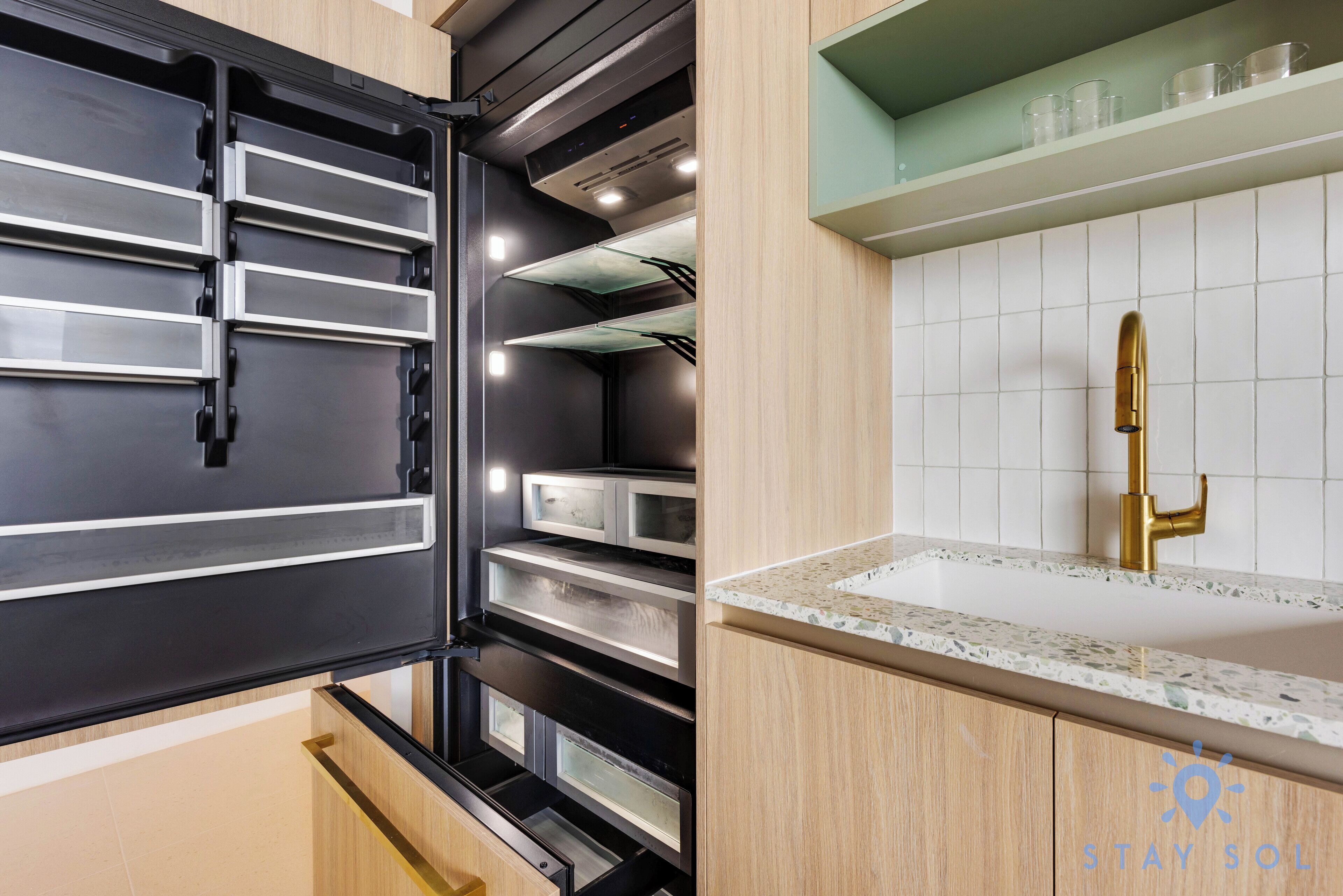Una cucina moderna con un frigorifero nero, un forno integrato e un piano di lavoro con un rubinetto dorato.