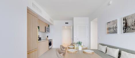 Una cocina moderna con armarios de madera, una mesa de comedor preparada para cuatro personas con platos y vasos, y un sofá gris con cojines.