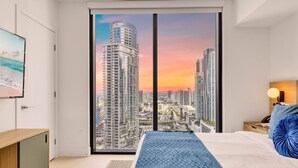 A modern hotel room with a large sliding glass door leading to a cityscape view at sunset. - Stay Sol Downtown (Miami)