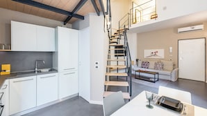 Eine moderne Küche mit weißen Schränken und einem eingebauten Backofen, ein Essbereich mit Tisch für zwei Personen und eine Treppe, die zu einer oberen Ebene führt.
