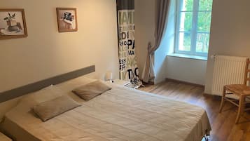 A bedroom with a large bed, a nightstand, a chair, a window with curtains, and two framed pictures on the wall.