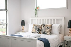 Een net opgemaakt bed met witte lakens en een gestreept kussen, met aan weerszijden nachtkastjes en lampen.