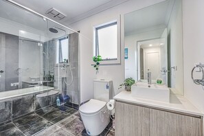 Een moderne badkamer met een glazen douchecabine, toilet, wastafel en grote spiegel.