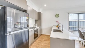 A modern kitchen with stainless steel appliances, a central island, and a view of the balcony. - StayAU Fresh Modern 5BR Retreat Netflix in Berwick (Berwick)