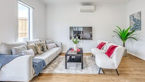A modern living room with a sofa, armchair, coffee table, and a flat-screen TV mounted on the wall. - StayAU Fresh Modern 5BR Retreat Netflix in Berwick (Berwick)