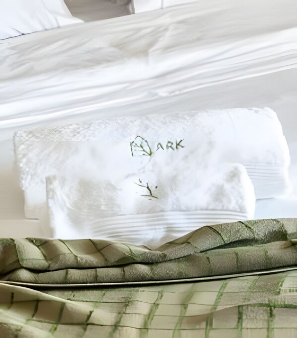 Una cama bien hecha con sábanas blancas y una manta verde a cuadros.