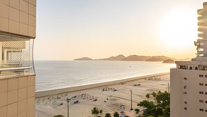 A coastal view from a high-rise building with a balcony overlooking a beach and distant mountains.