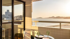 A balcony with a view of the sea and mountains, a table with plates and glasses, and a chair.