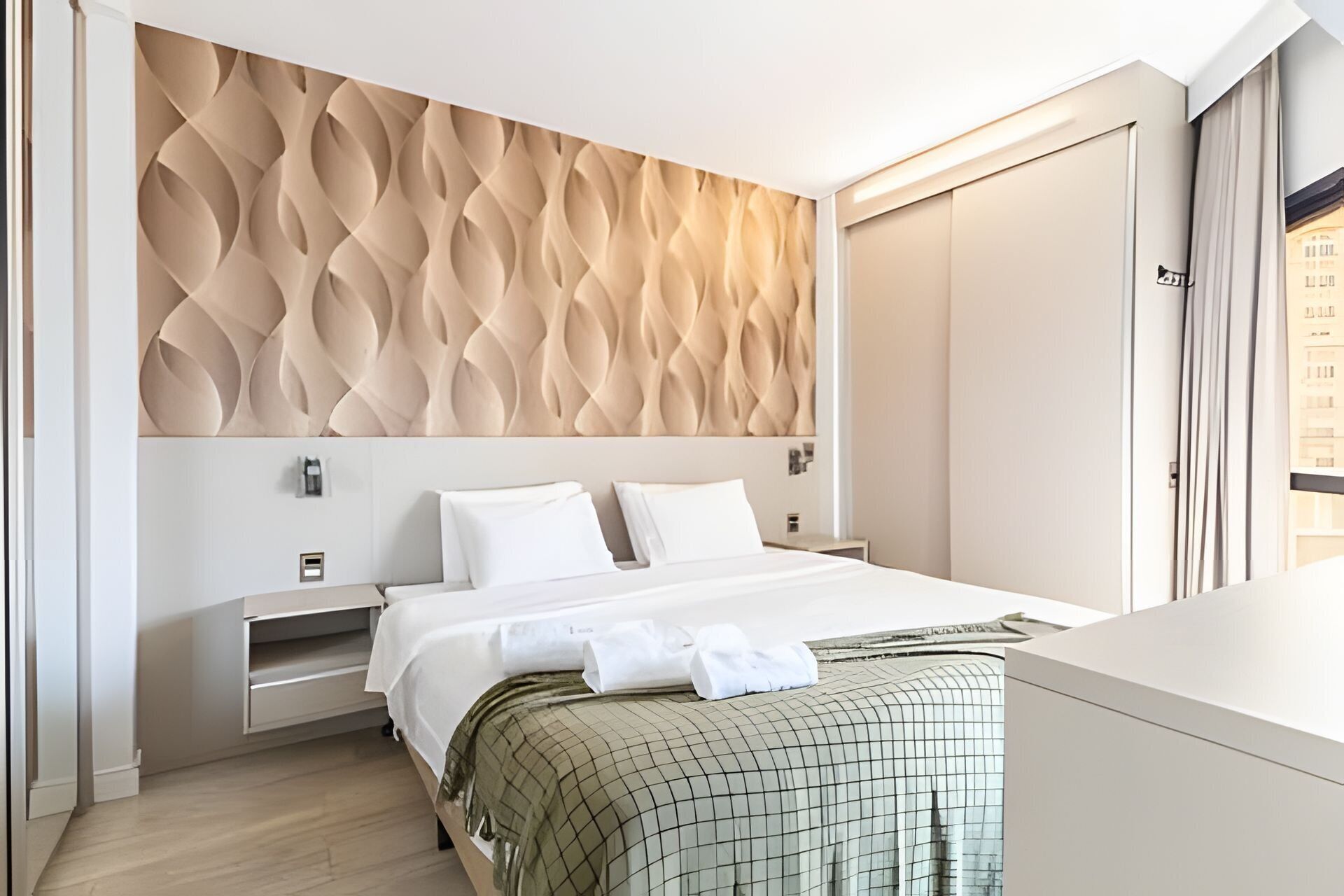 Un dormitorio moderno con cama, mesitas de noche, armario y vistas a un edificio.